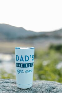 Close-up of a dad-themed tumbler on a rock outdoors, with blurred natural background.