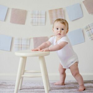 Cute baby standing by a stool indoors with a playful background.
