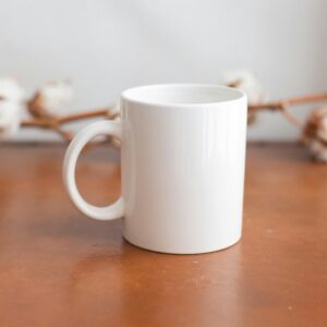 Minimalist white mug on a wooden surface with cotton flowers in the background, ideal for mockups.